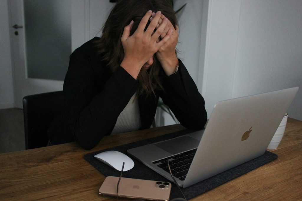 A frustrated person facepalming at their laptop. 